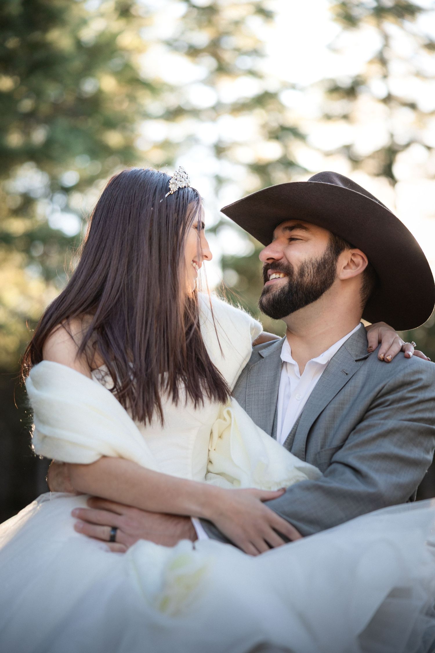 Intimate wedding portrait with cowboy hat and white dress in forest setting.