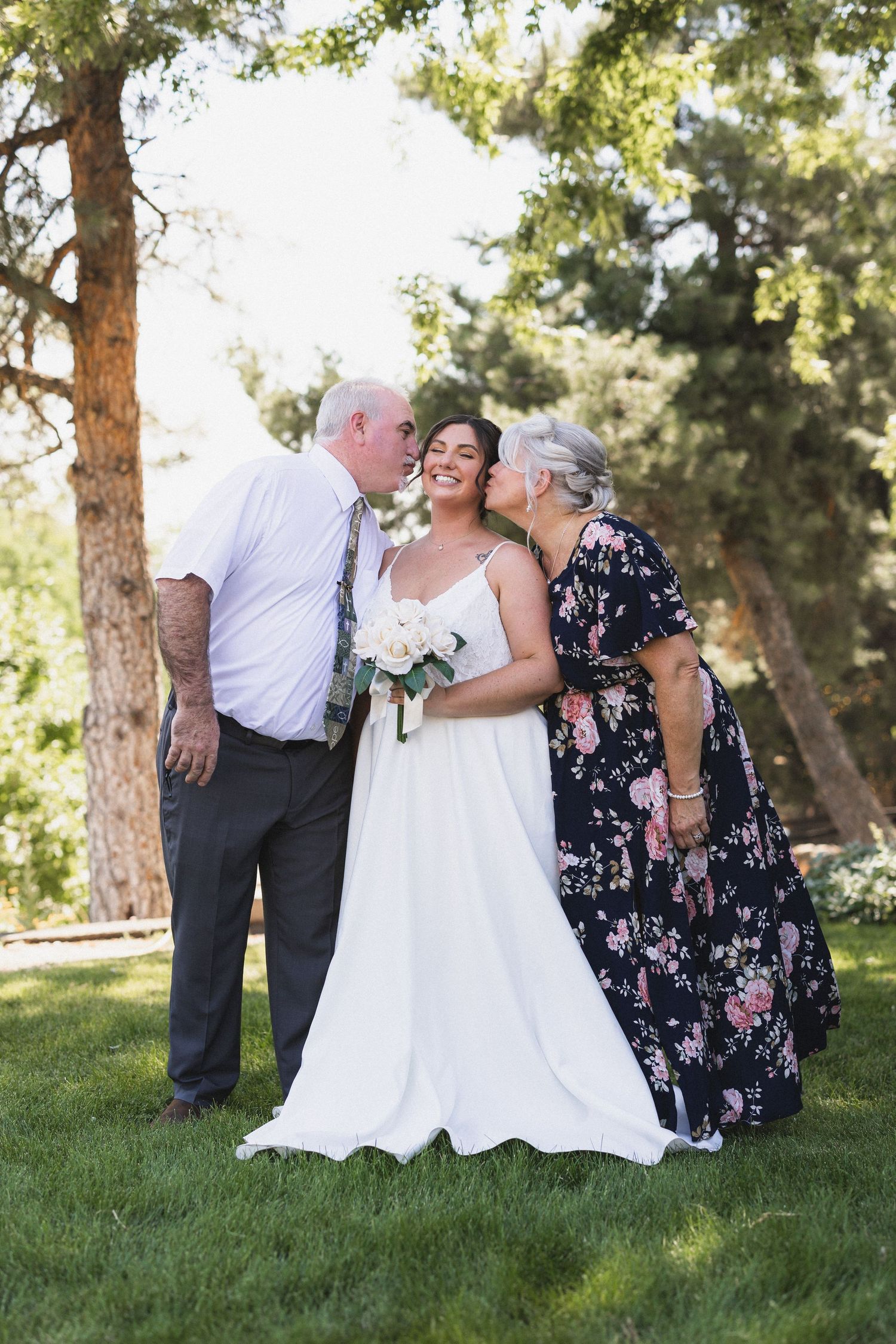 Outdoor wedding photo with bride in white dress surrounded by evergreen trees.