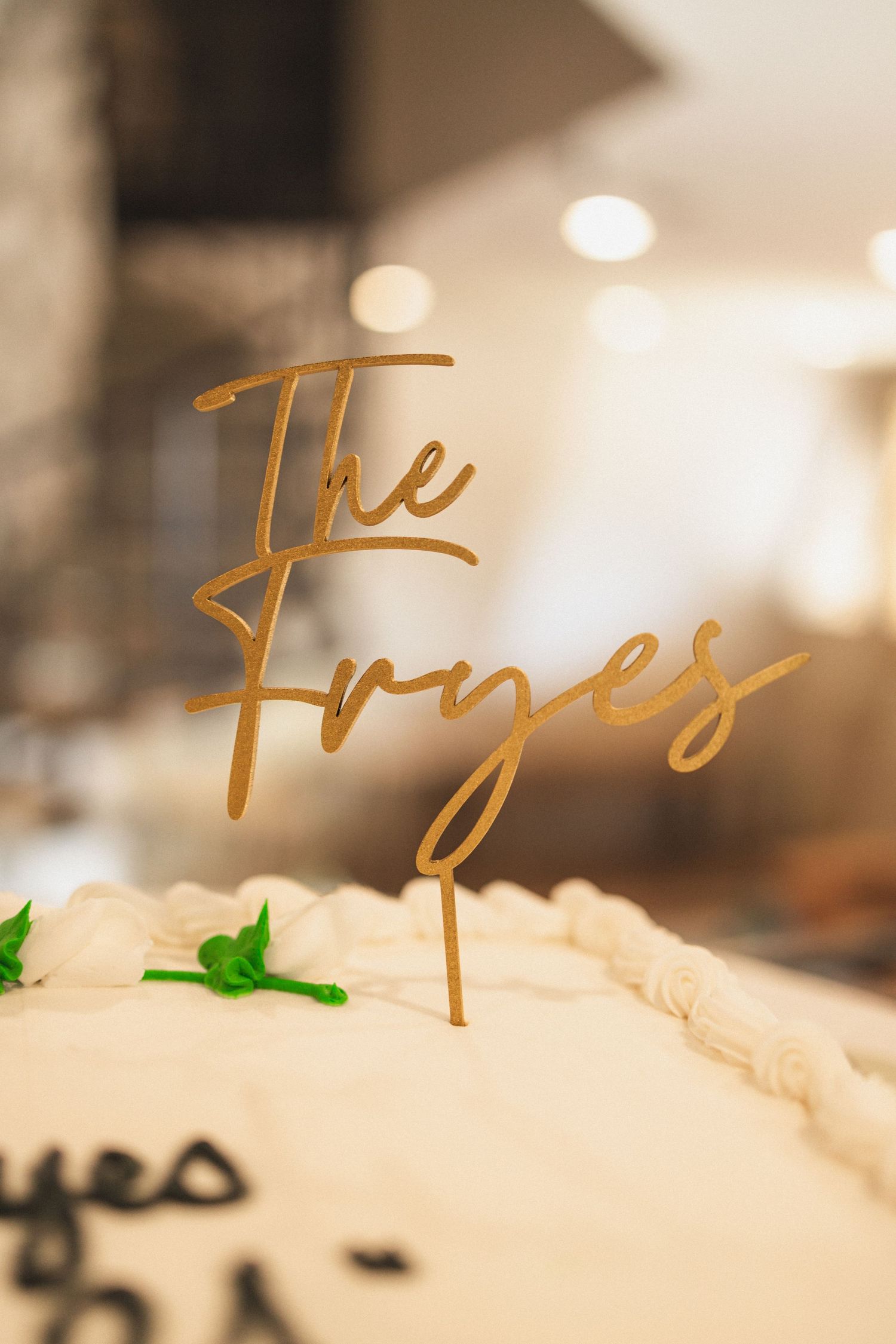 Gold cake topper reading 'The Fryes' decorates a wedding cake with elegant styling.