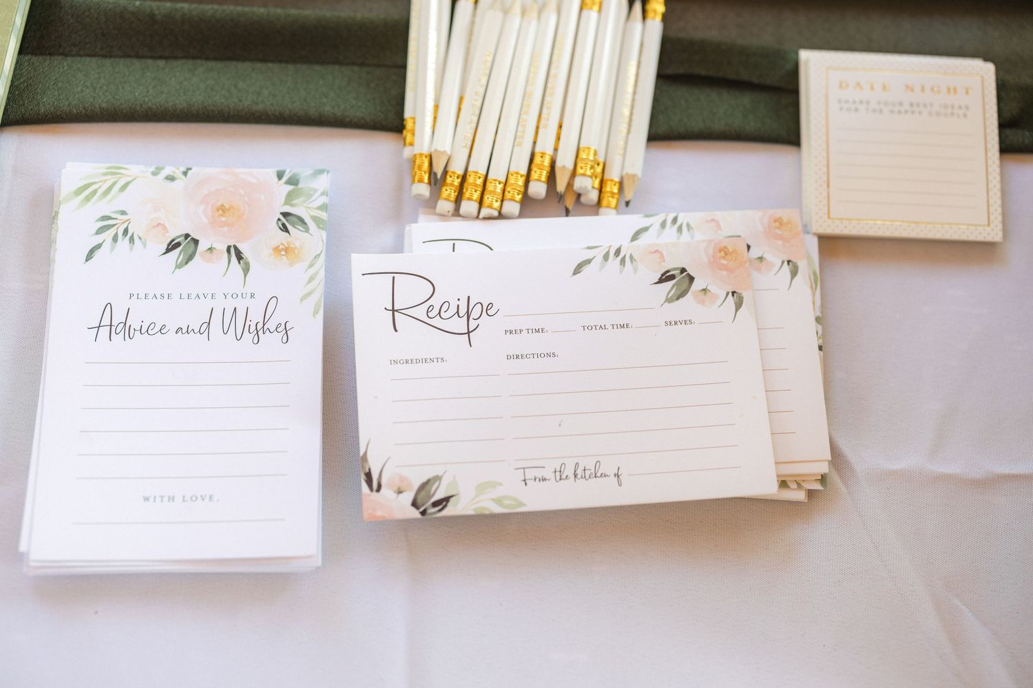 Wedding stationery with floral designs and pencils arranged on a white tablecloth.