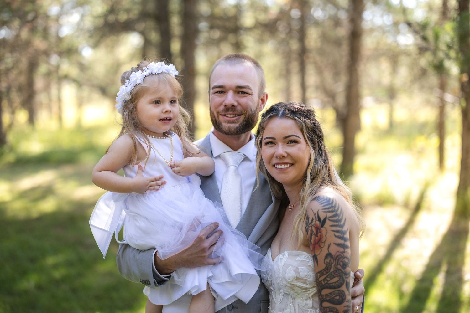 Joyful family wedding portrait captured in a sunny forest setting.