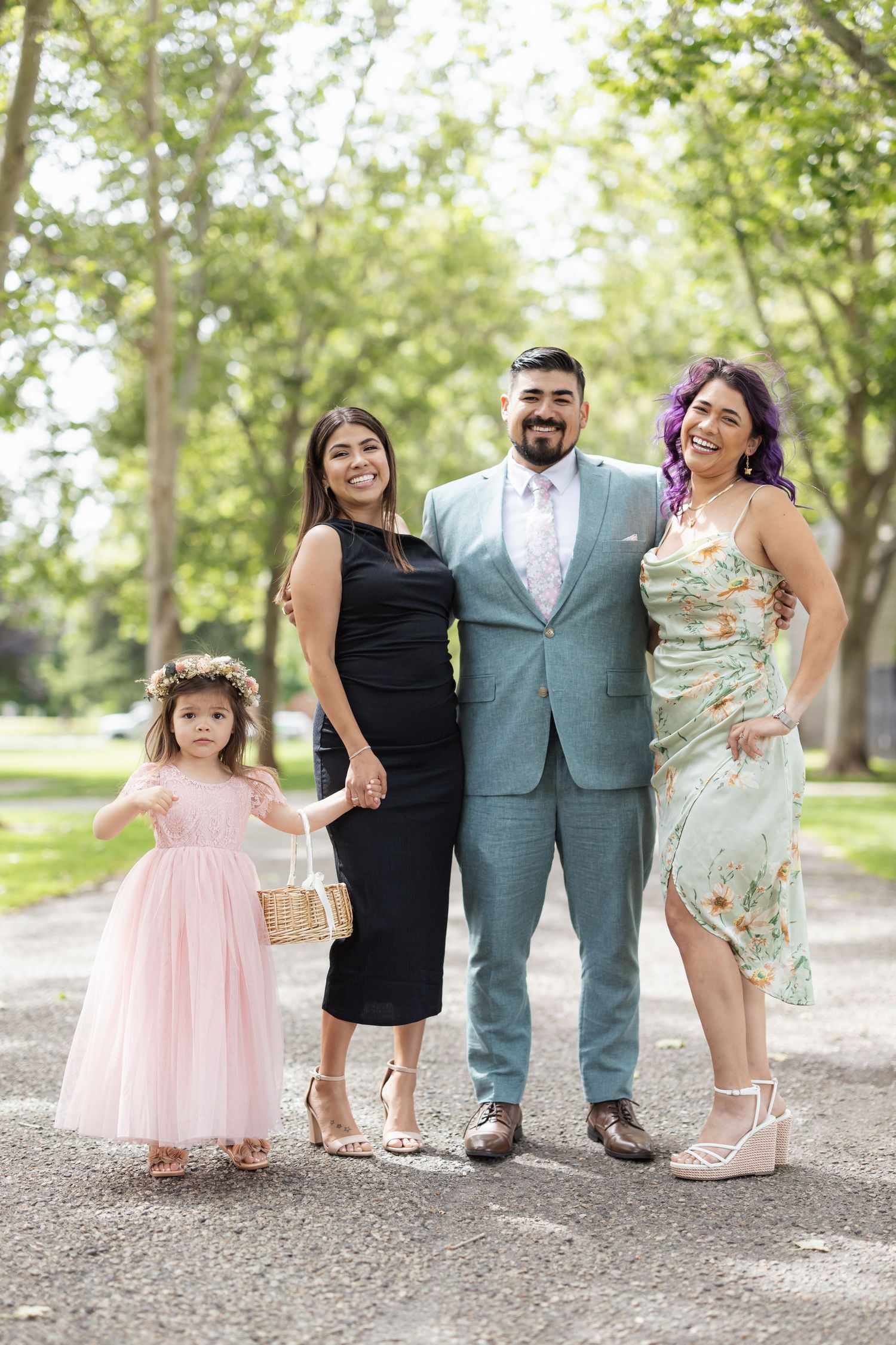 Wedding group photo with flower girl, two women, and man in light blue suit on garden path.