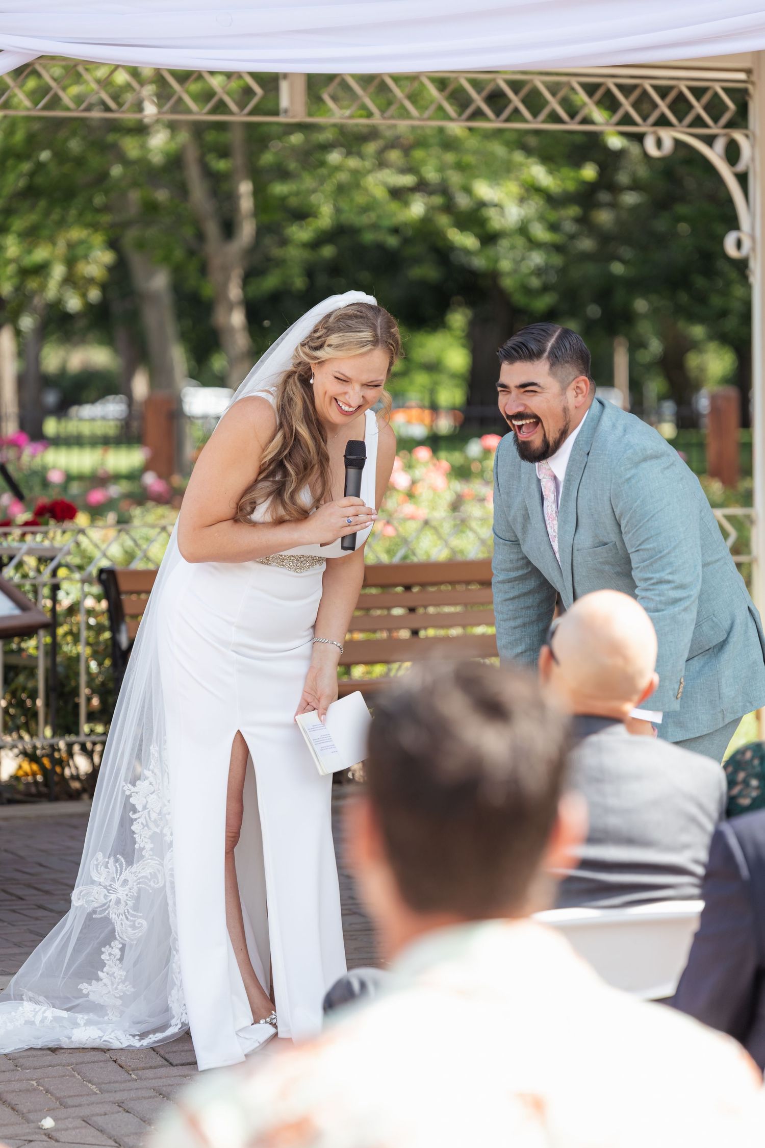 Happy couple laughing during outdoor wedding ceremony under decorative gazebo.