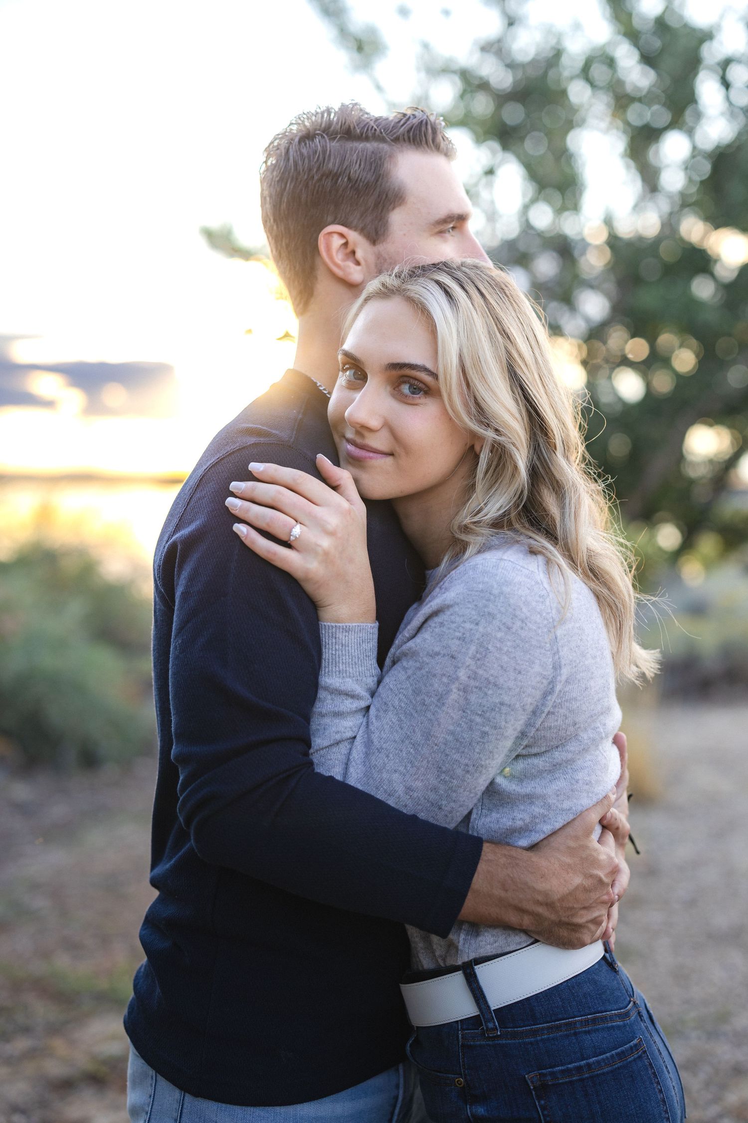 Romantic couple embracing during golden hour photoshoot in a natural outdoor setting.