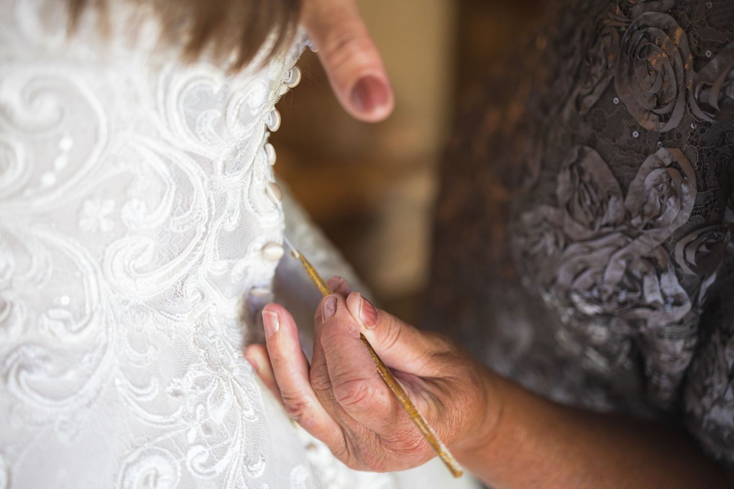 Hands adjusting intricate lace details on white wedding dress fabric.