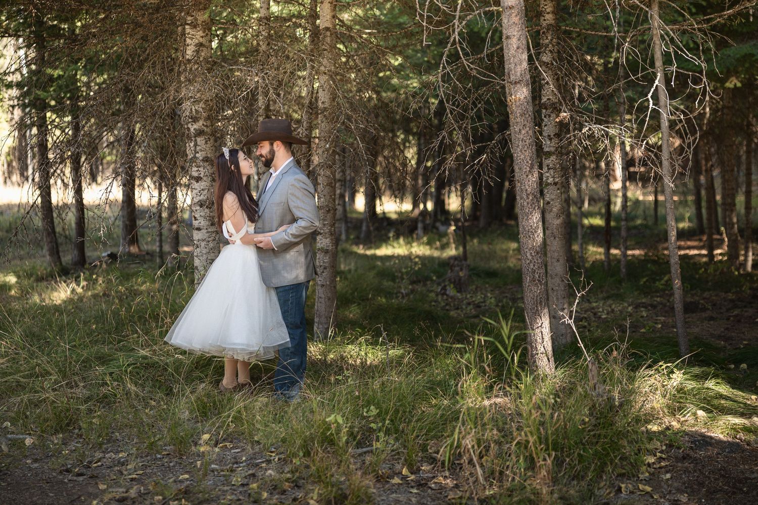 Newlyweds share an intimate moment surrounded by trees in a sunlit woodland.