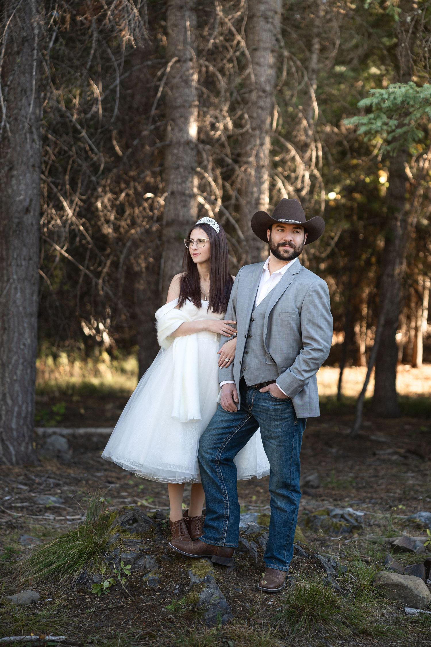 Couple in wedding attire poses romantically among forest trees.