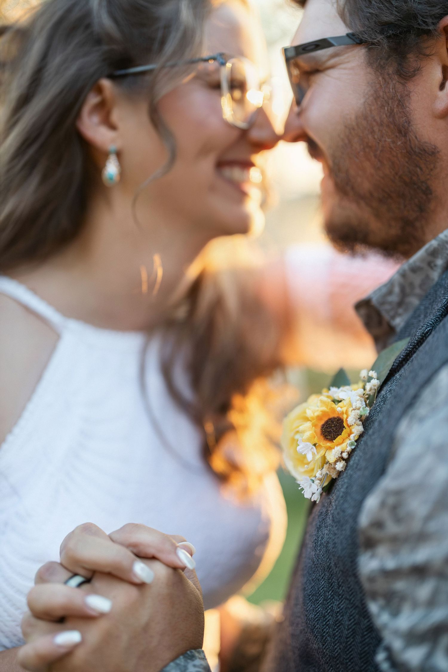 Intimate wedding moment captured in golden sunlight with sunflower boutonniere detail.