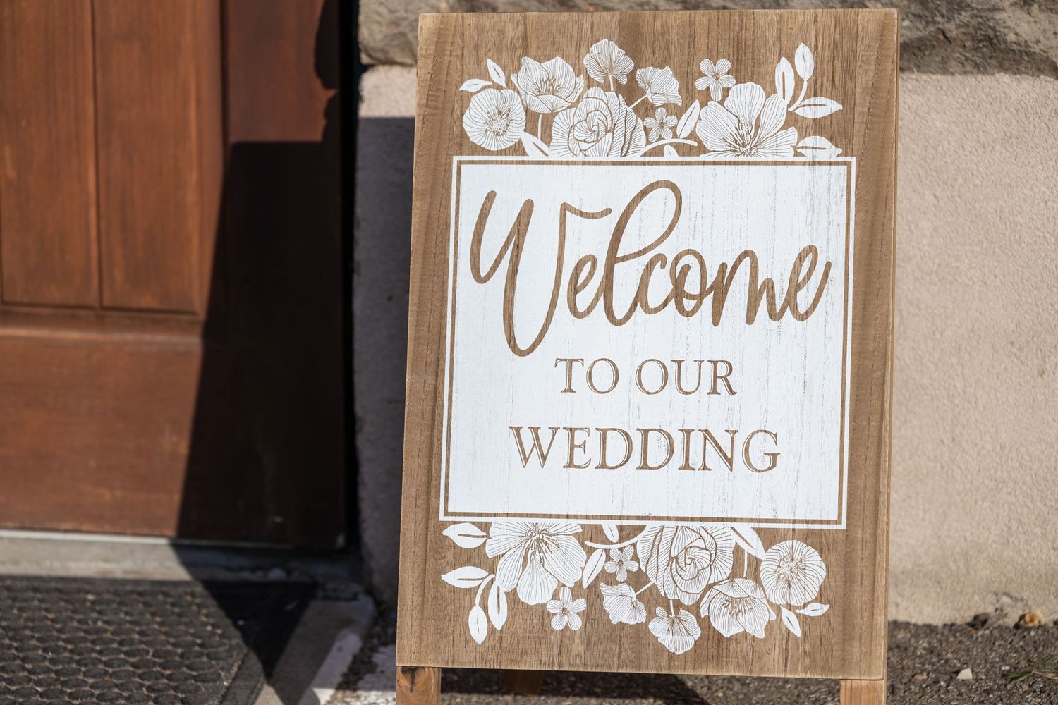 Rustic wooden welcome sign with floral details announces wedding celebration.