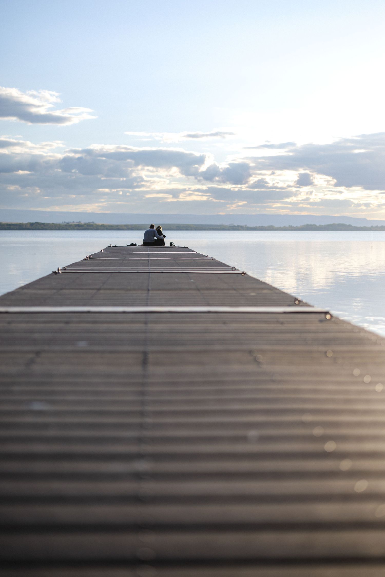 Long wooden dock stretches out over calm lake waters at sunset.