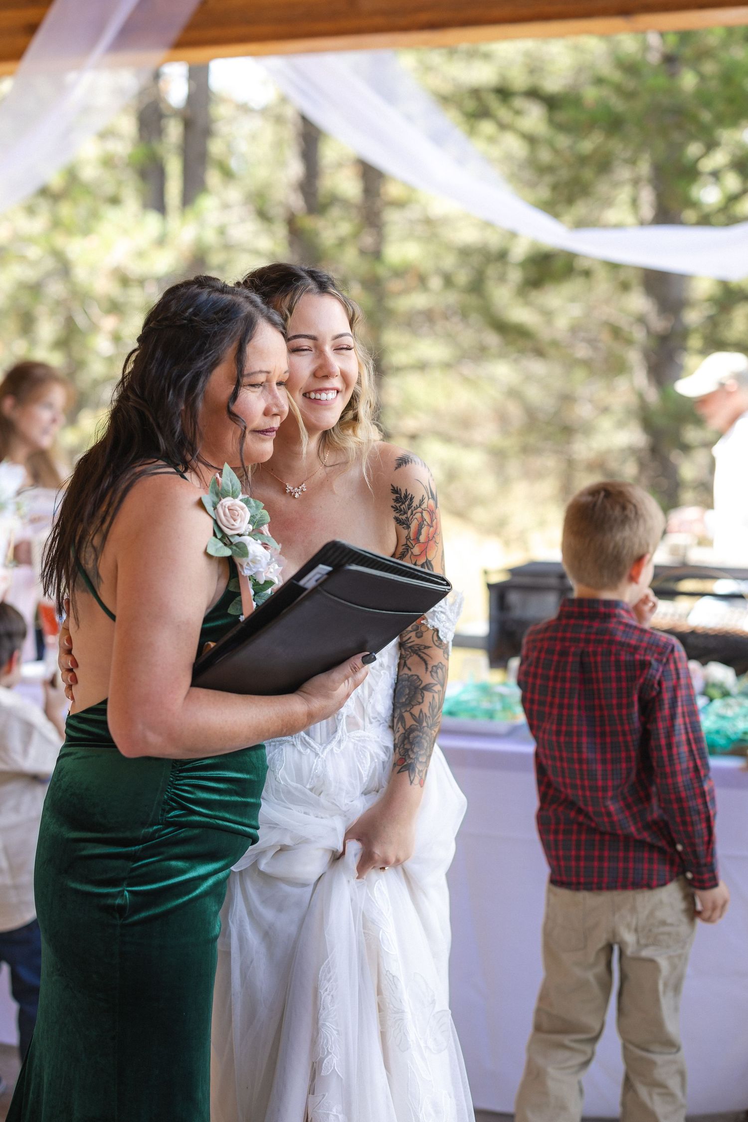 Two attendees in formal attire share joyful moment at outdoor wedding reception.