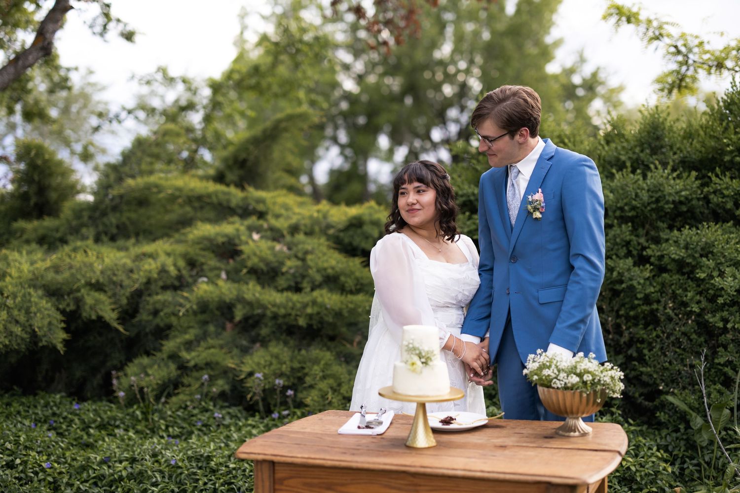 Couple shares intimate moment at wooden dessert table during garden wedding.