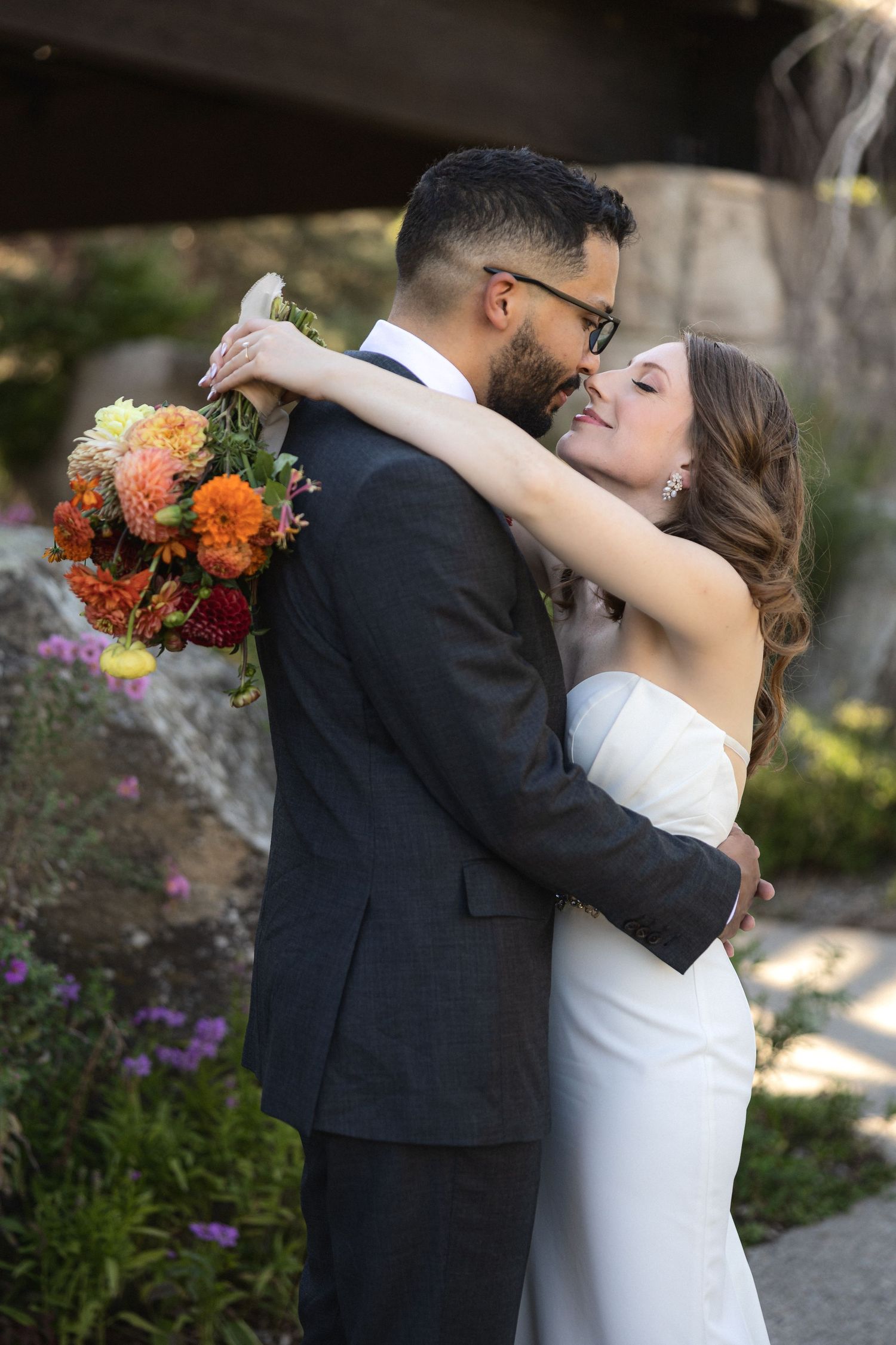 Newlyweds share an intimate moment with autumn-colored floral bouquet during outdoor wedding photos.
