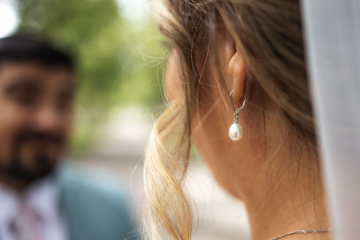 Detail shot of pearl drop earring with soft focus wedding scene in background.