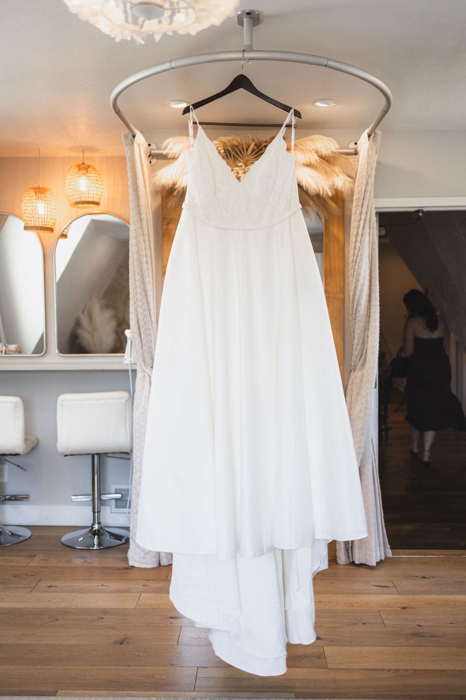Elegant white wedding dress with sweetheart neckline hanging on display in a bridal boutique with chandelier lighting.