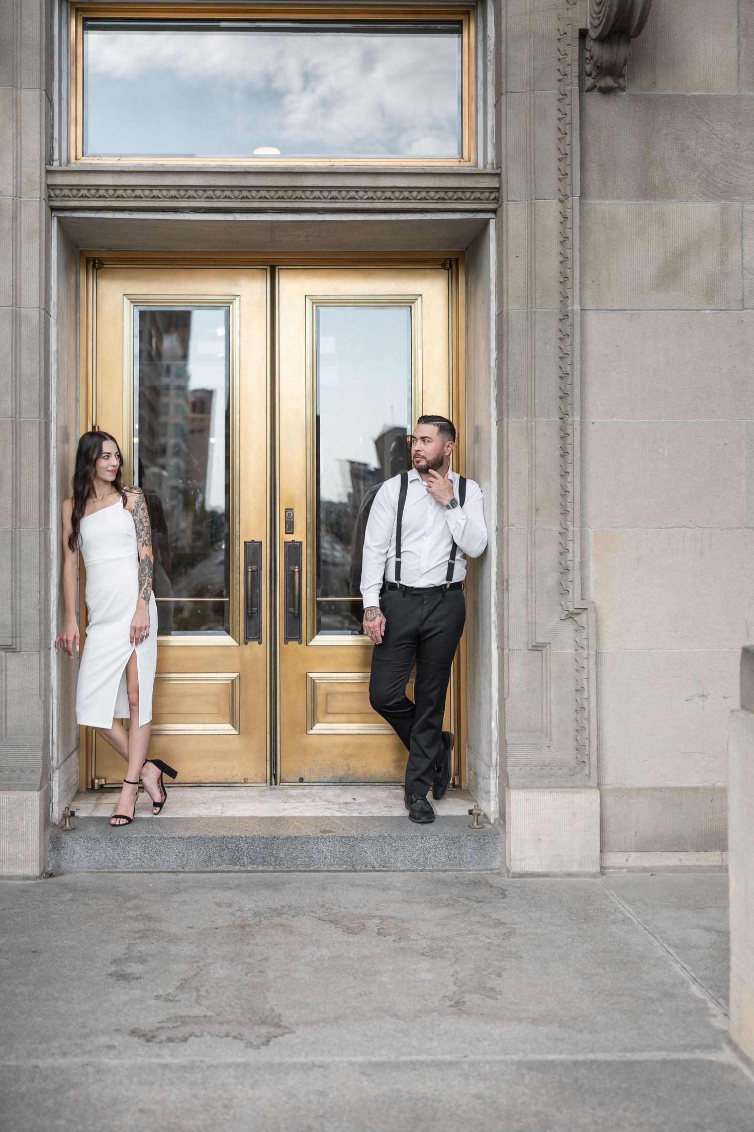 Elegant couple poses near golden doors of a historic building during a formal photo session.