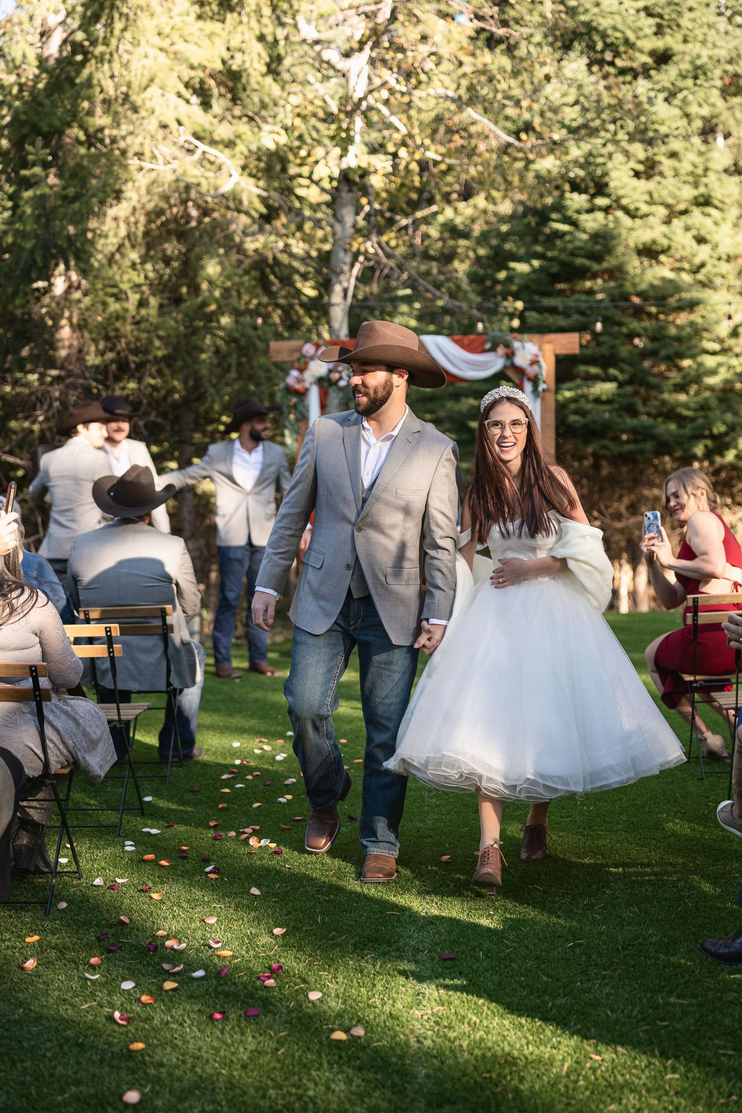 Wedding party dancing and celebrating on grass lawn during outdoor reception.