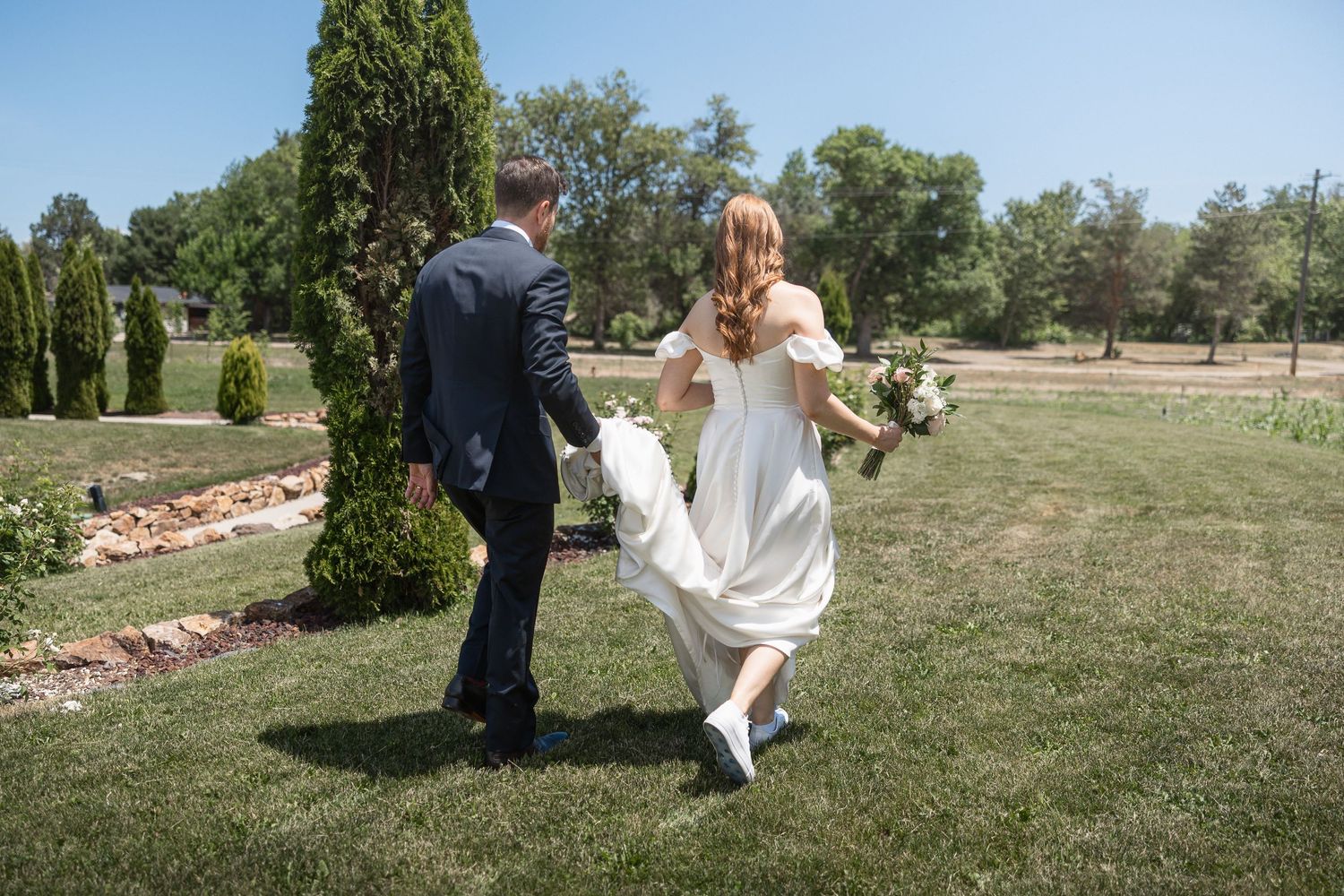 A couple walks together on manicured grass near landscaped gardens.