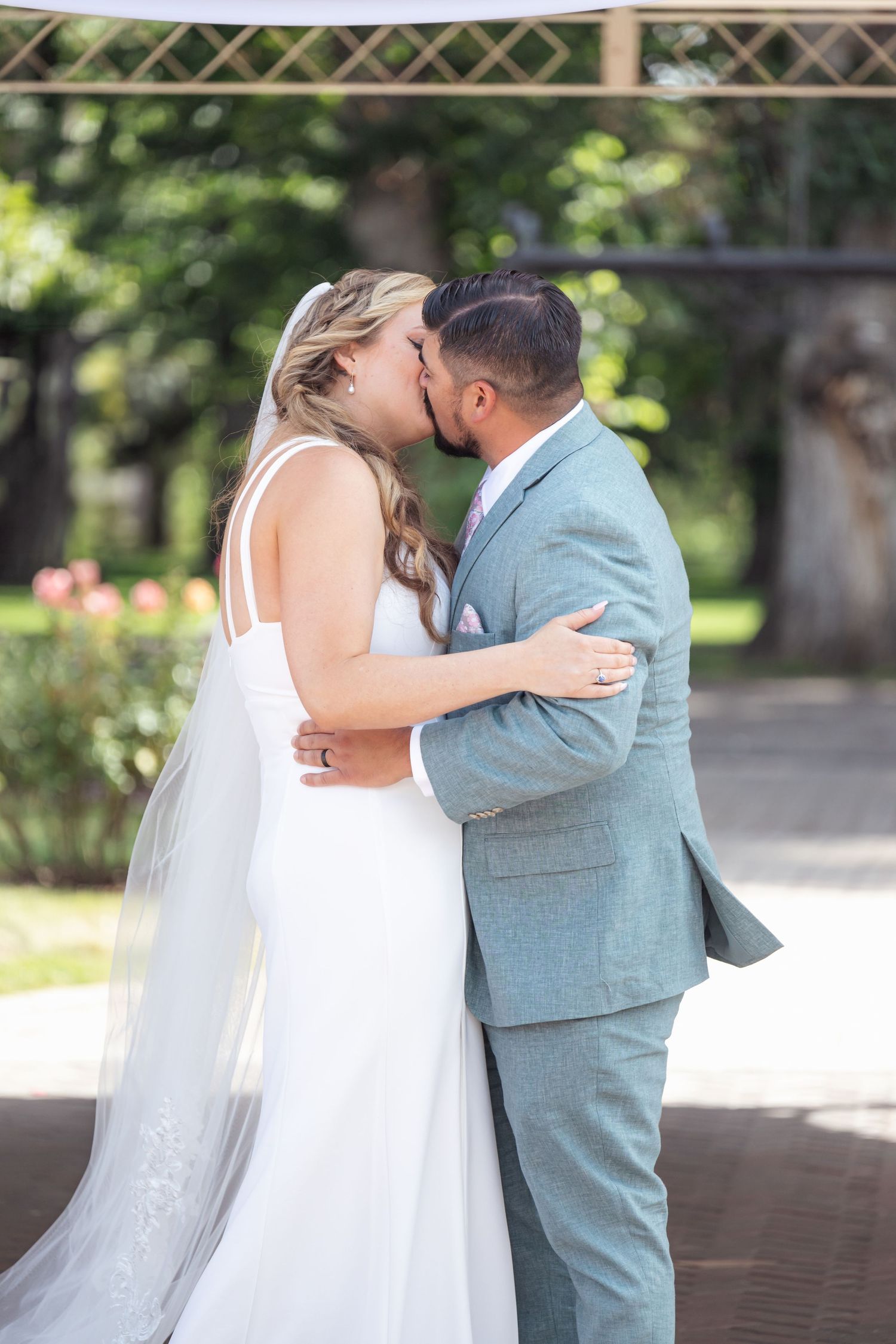 Newlyweds share their first kiss under decorated outdoor gazebo.