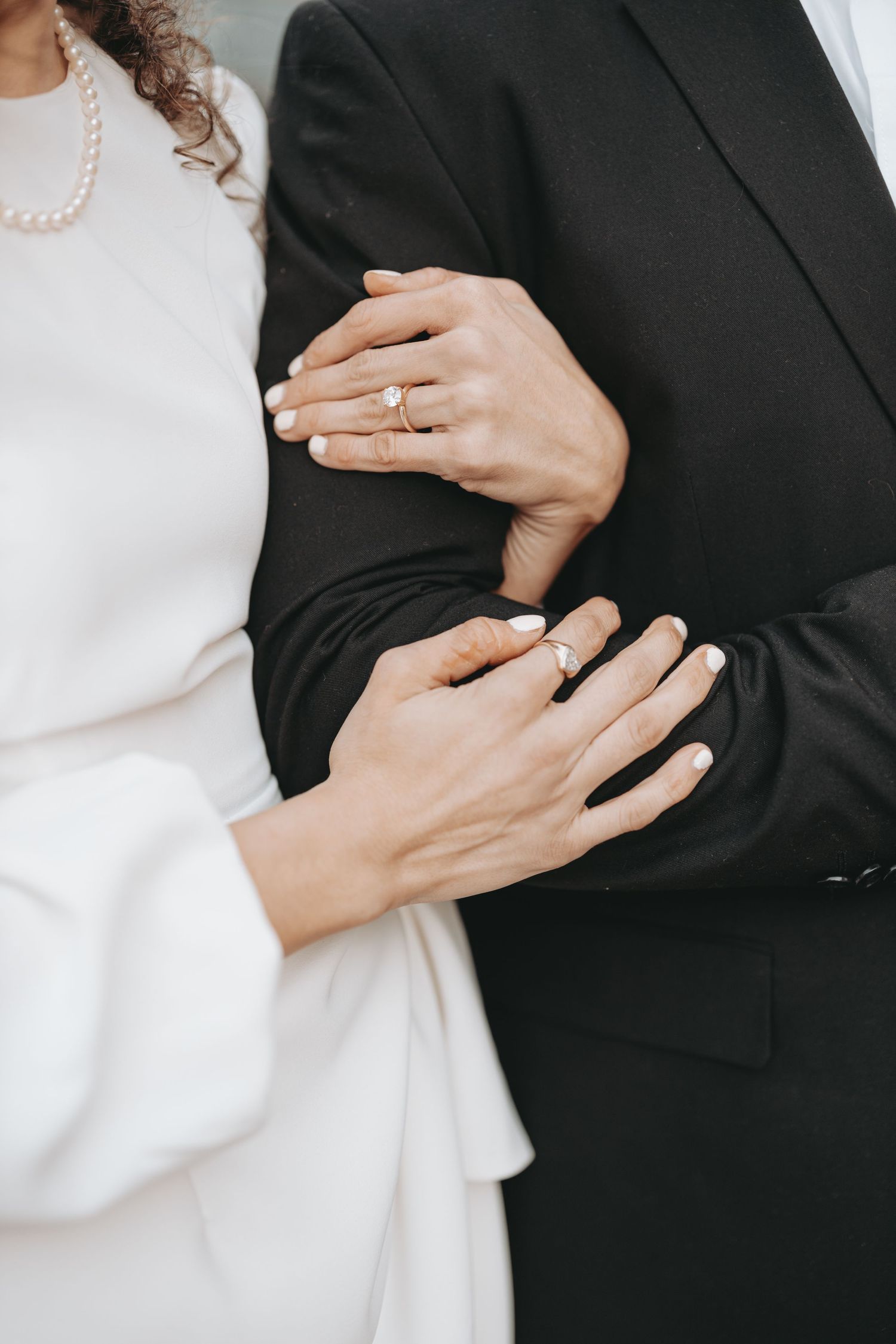 Close-up of hands with engagement rings against formal black and white attire.