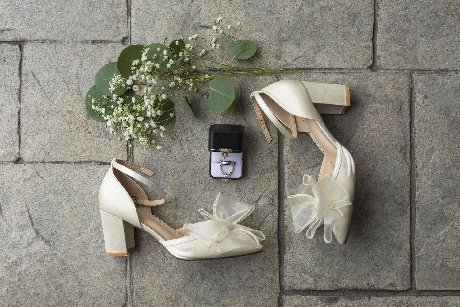 Bridal shoes and ring box styled with delicate baby's breath on stone pavers.