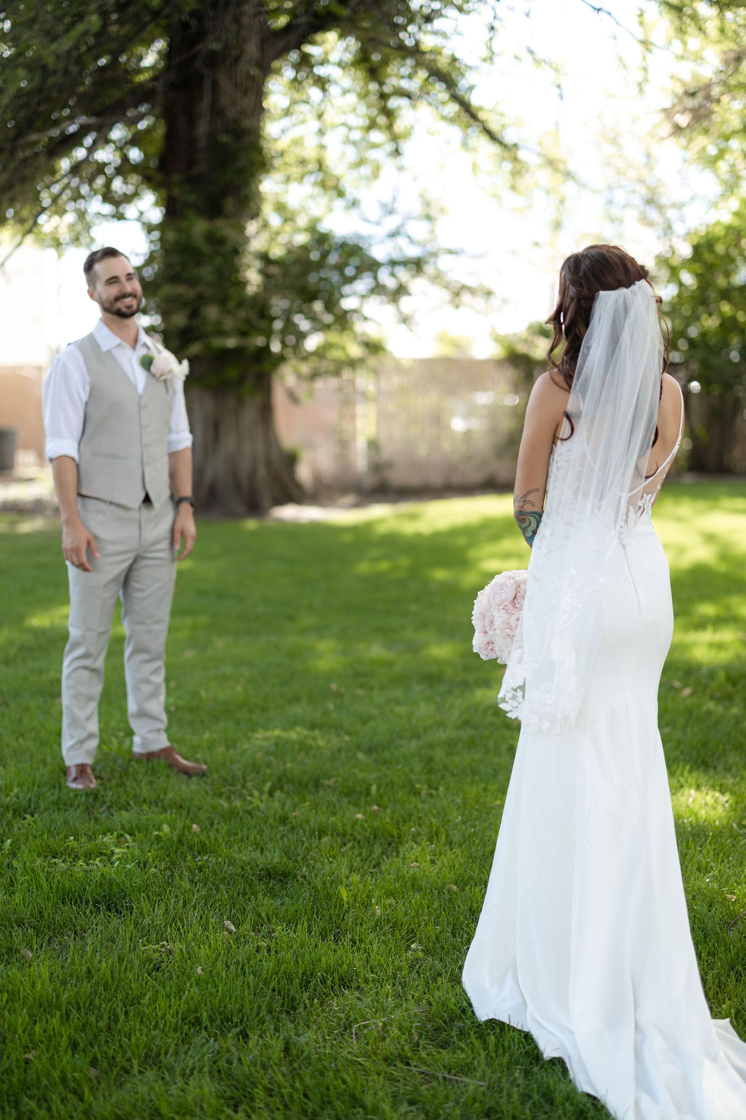 Wedding couple standing apart on grass with bride's flowing veil and dress in foreground.
