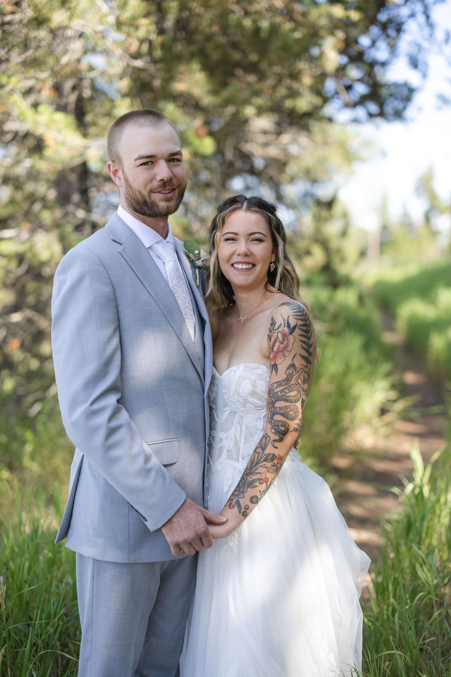 Happy couple in wedding attire laughs together in a forest clearing.