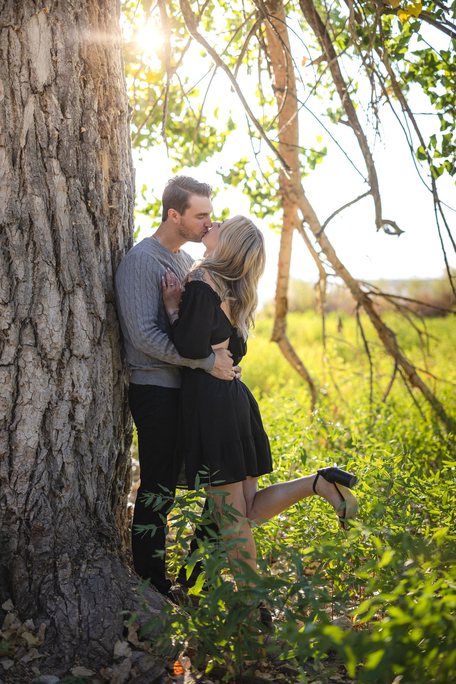 Romantic sunset portrait of couple embracing against large tree trunk.