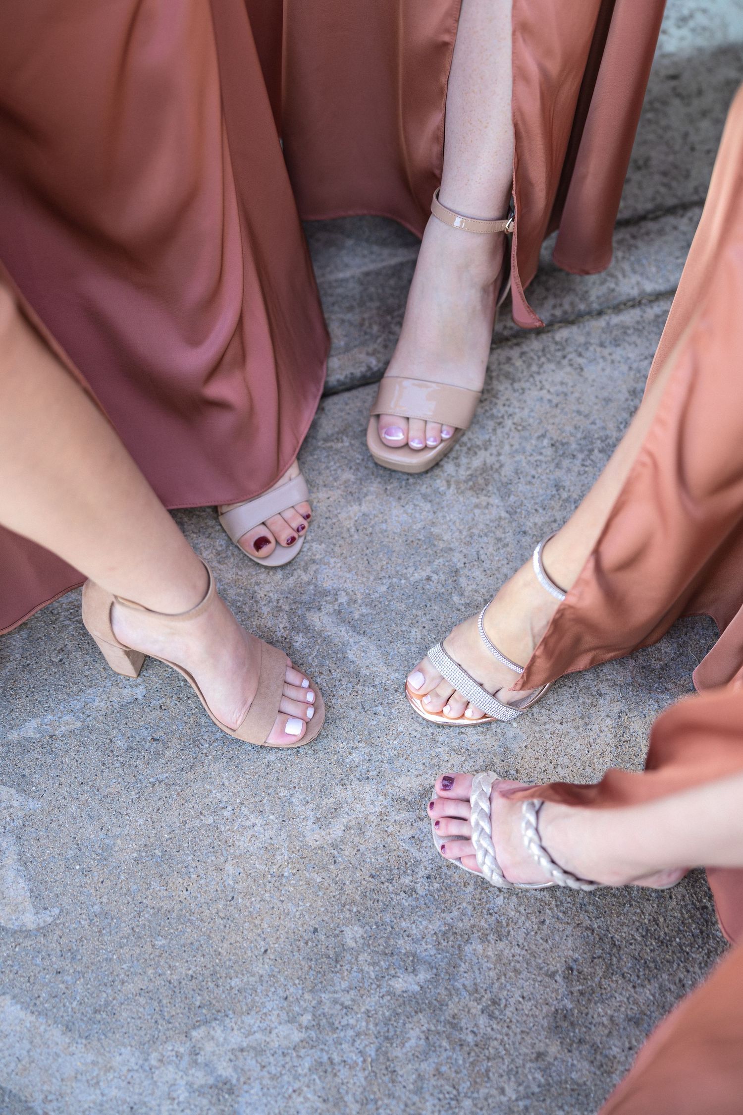 Bridesmaids in dusty rose dresses showing their matching nude strappy sandals on stone ground.
