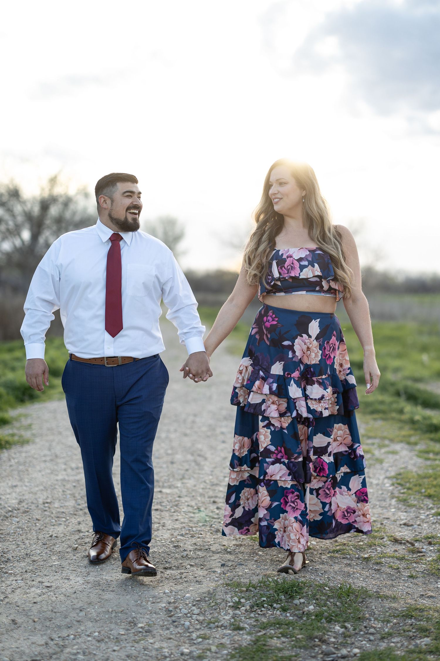 Couple walking hand in hand on a gravel path in coordinated formal attire.