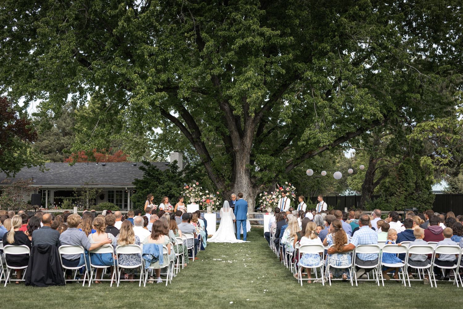 White chairs arranged in rows for an outdoor wedding ceremony under tall green trees.