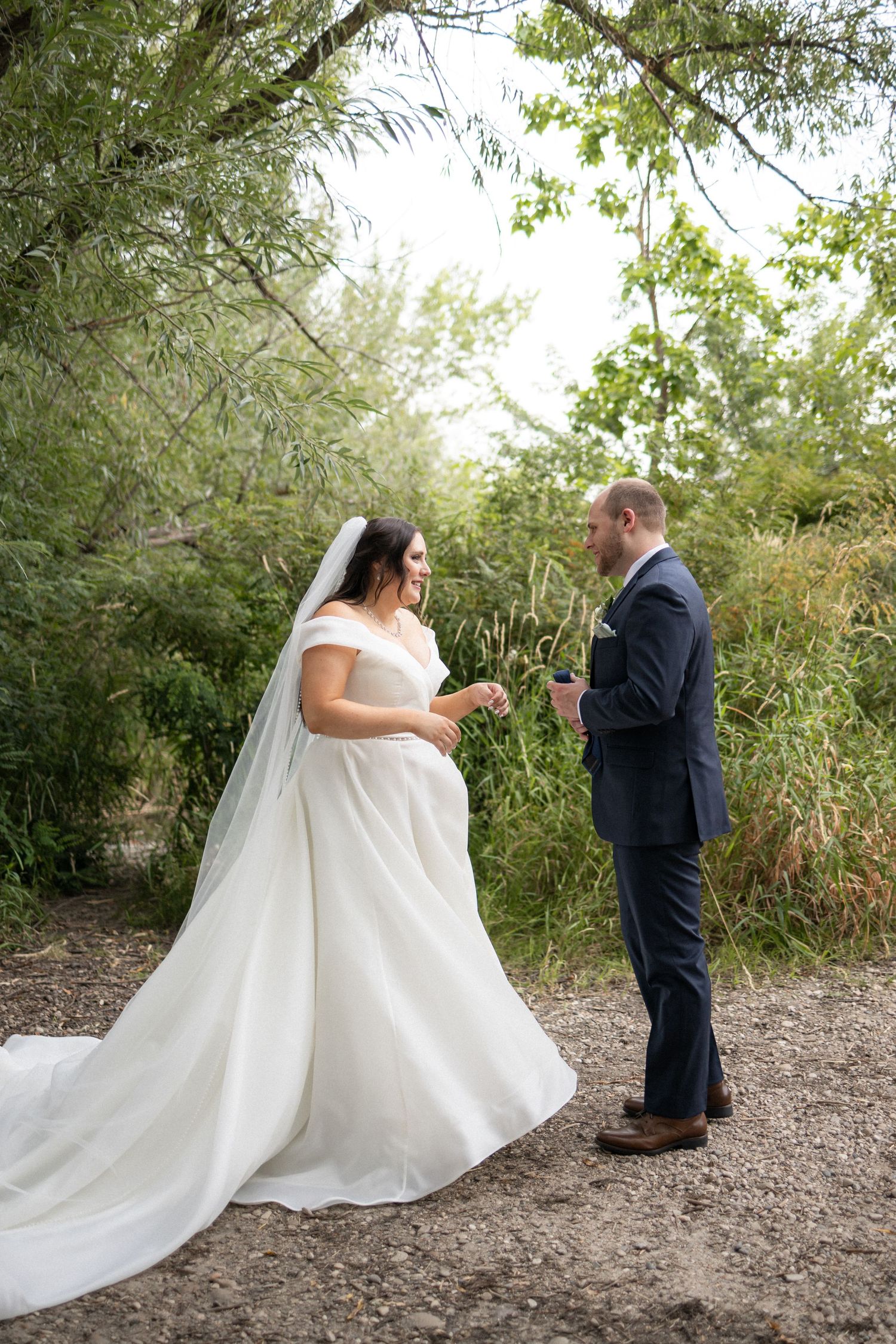 A couple engages in their first look wedding moment on a natural dirt path surrounded by trees.