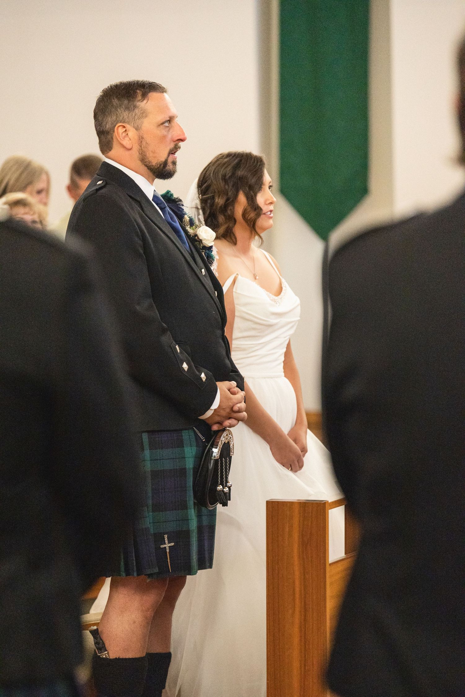 Wedding ceremony with couple standing at altar, groom wearing traditional Scottish kilt.