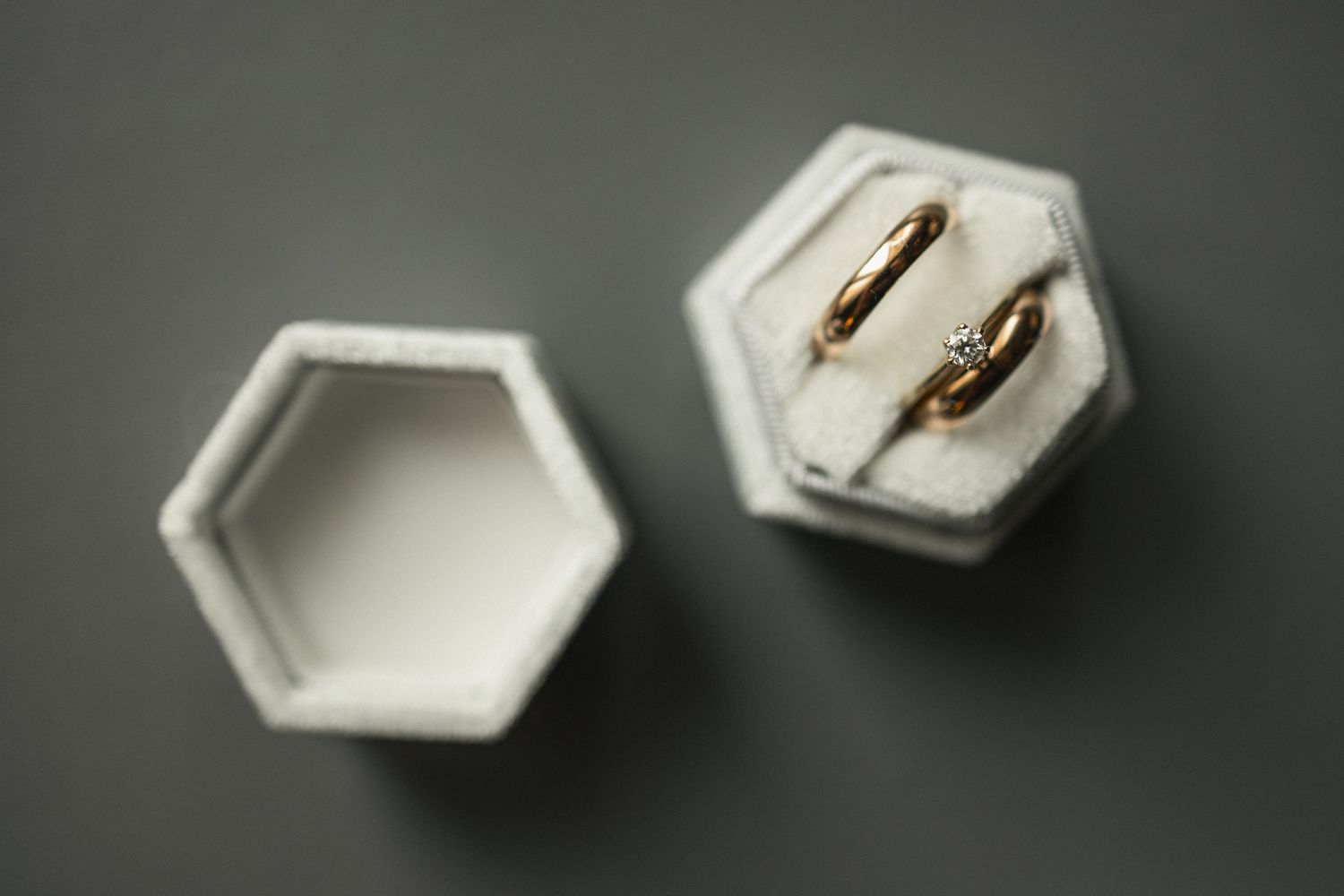 Two gold wedding bands displayed in white hexagonal ring box on dark surface.