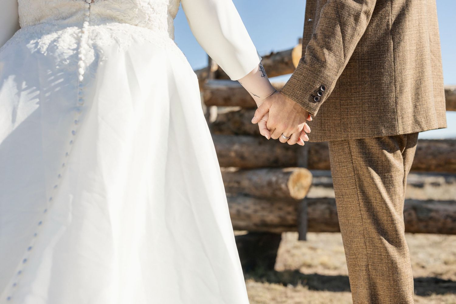 Close-up details of wedding attire showing white dress and brown suit in outdoor setting.