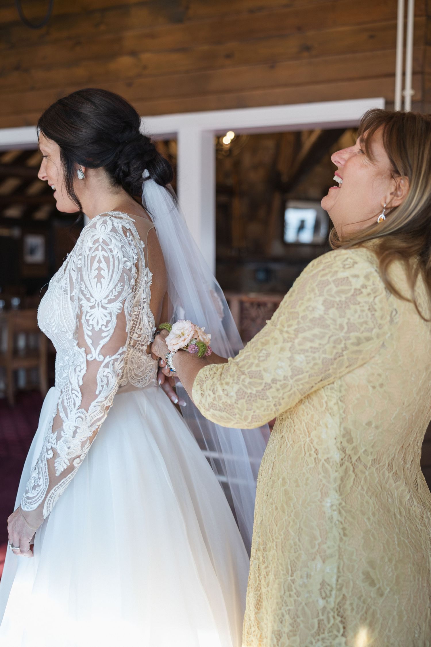 Wedding dress with delicate lace sleeves next to yellow dress in wooden venue.