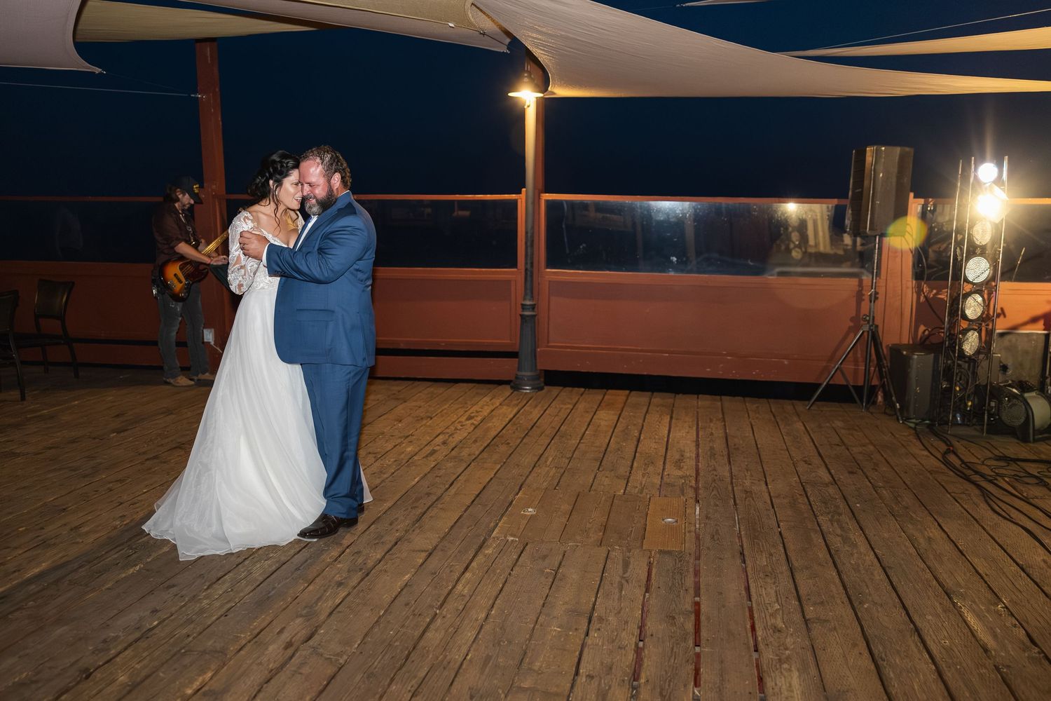 Couple dancing under candlelit canopy on wooden deck at night.