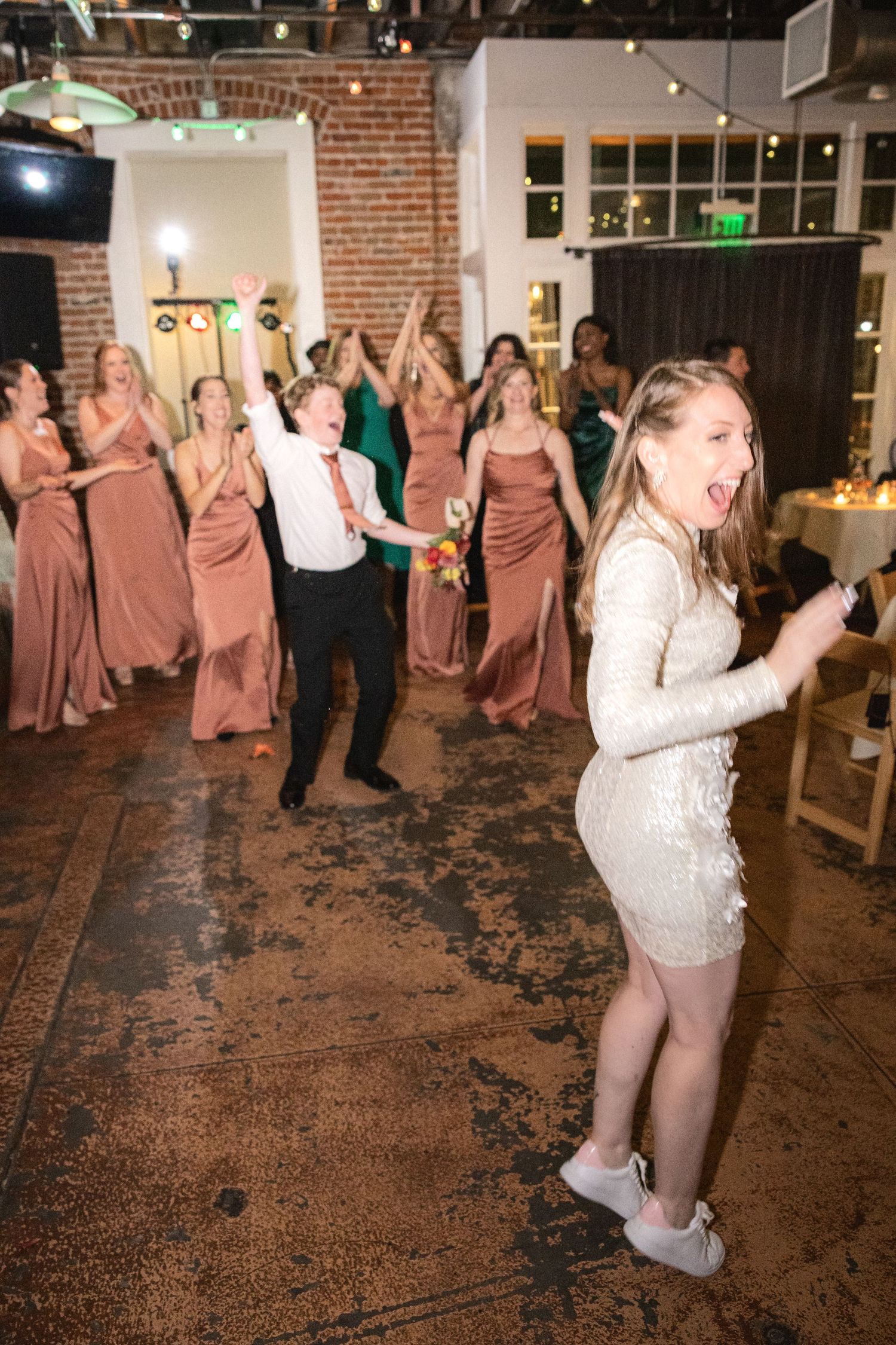People dancing and celebrating on a rustic brick floor at a wedding reception.