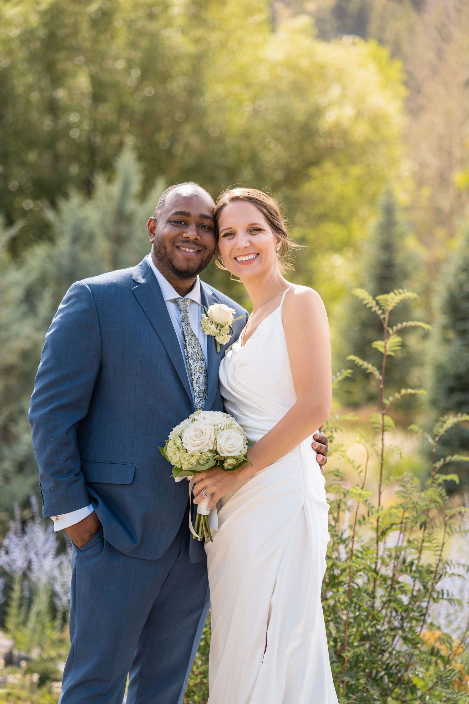 A romantic wedding photoshoot in a garden with a couple in formal attire against golden sunlight.