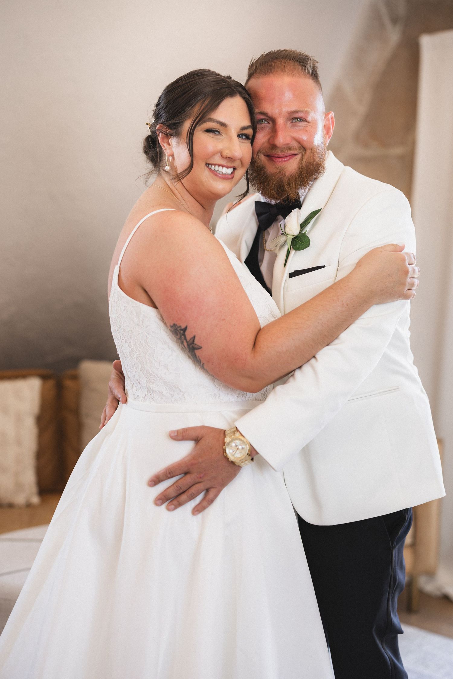 Happy wedding couple embracing in a sunlit room with stone walls.
