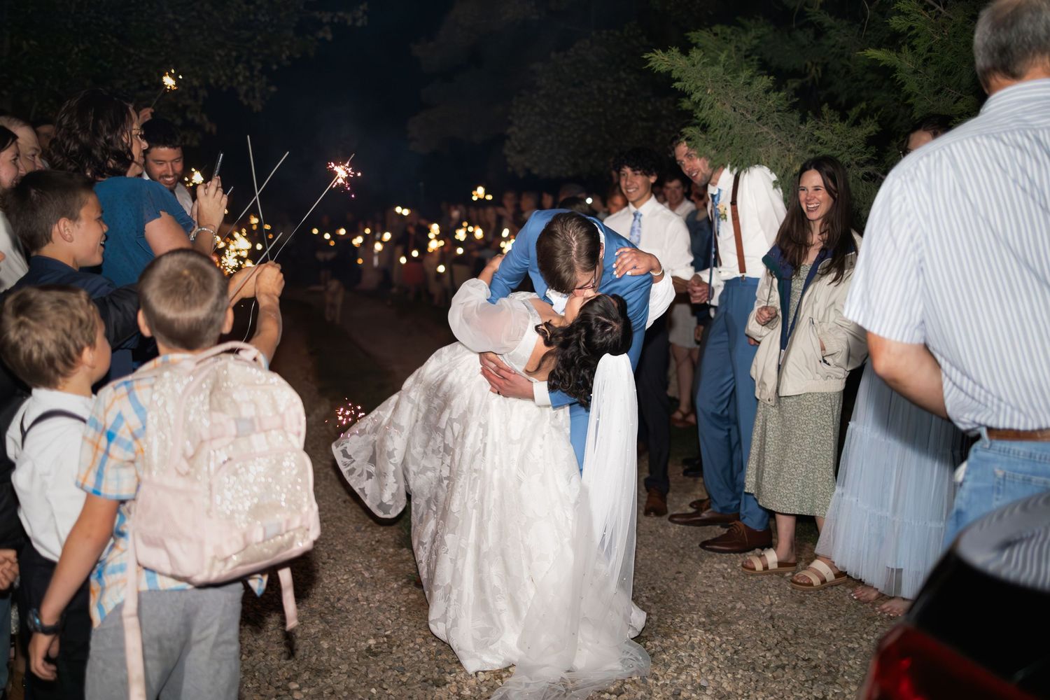 Festive nighttime gathering with guests holding sparklers under dark skies.