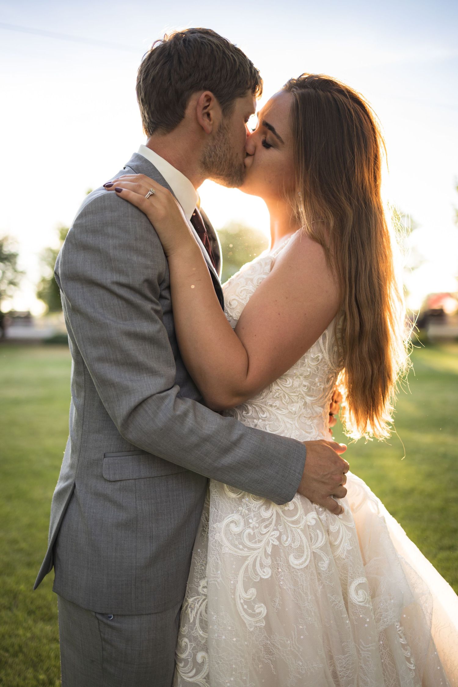 A romantic wedding kiss captured in warm sunset lighting on a summer evening.