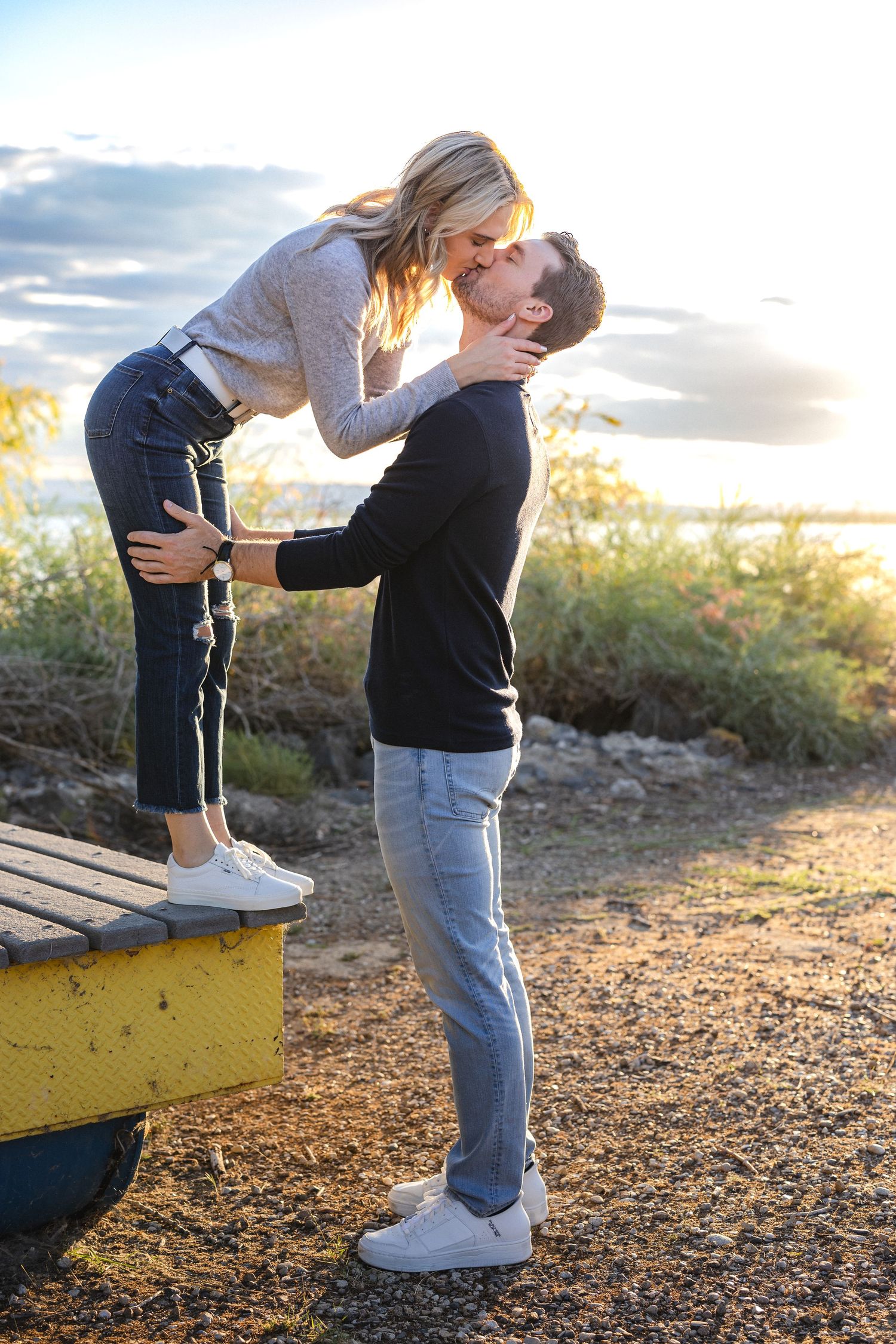 Romantic sunset moment with lifted embrace on a yellow platform by the water.