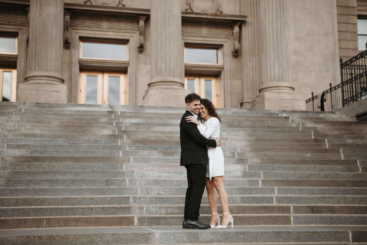 A couple embraces on stone steps of a historic building with columns.