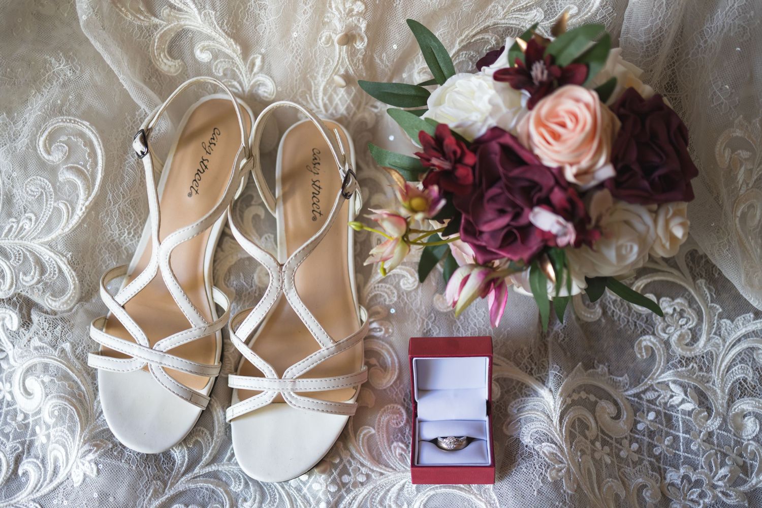 Wedding details including white strappy sandals, floral bouquet, and engagement ring in red box.