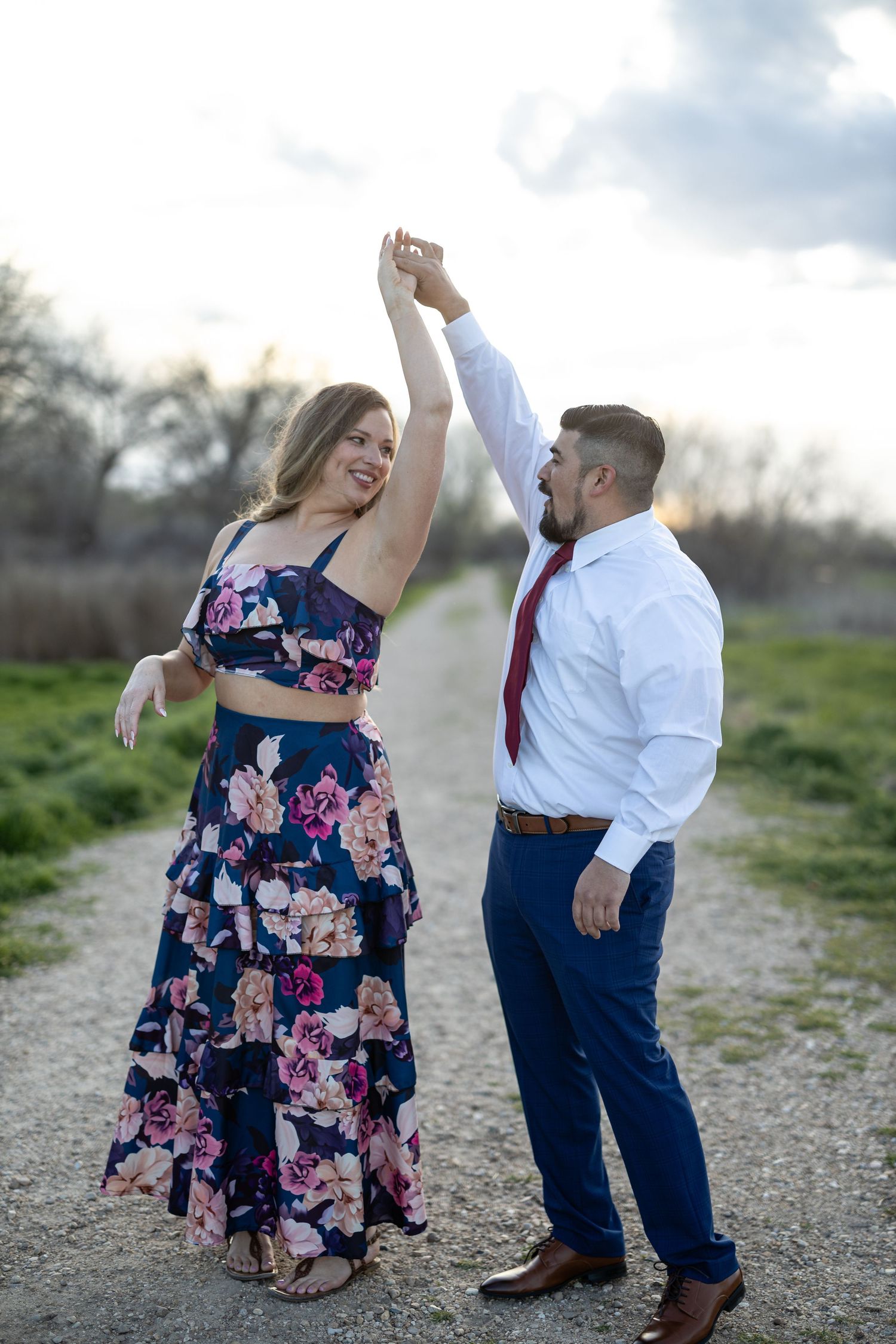 Couple dancing and twirling on outdoor path with green hillside backdrop.