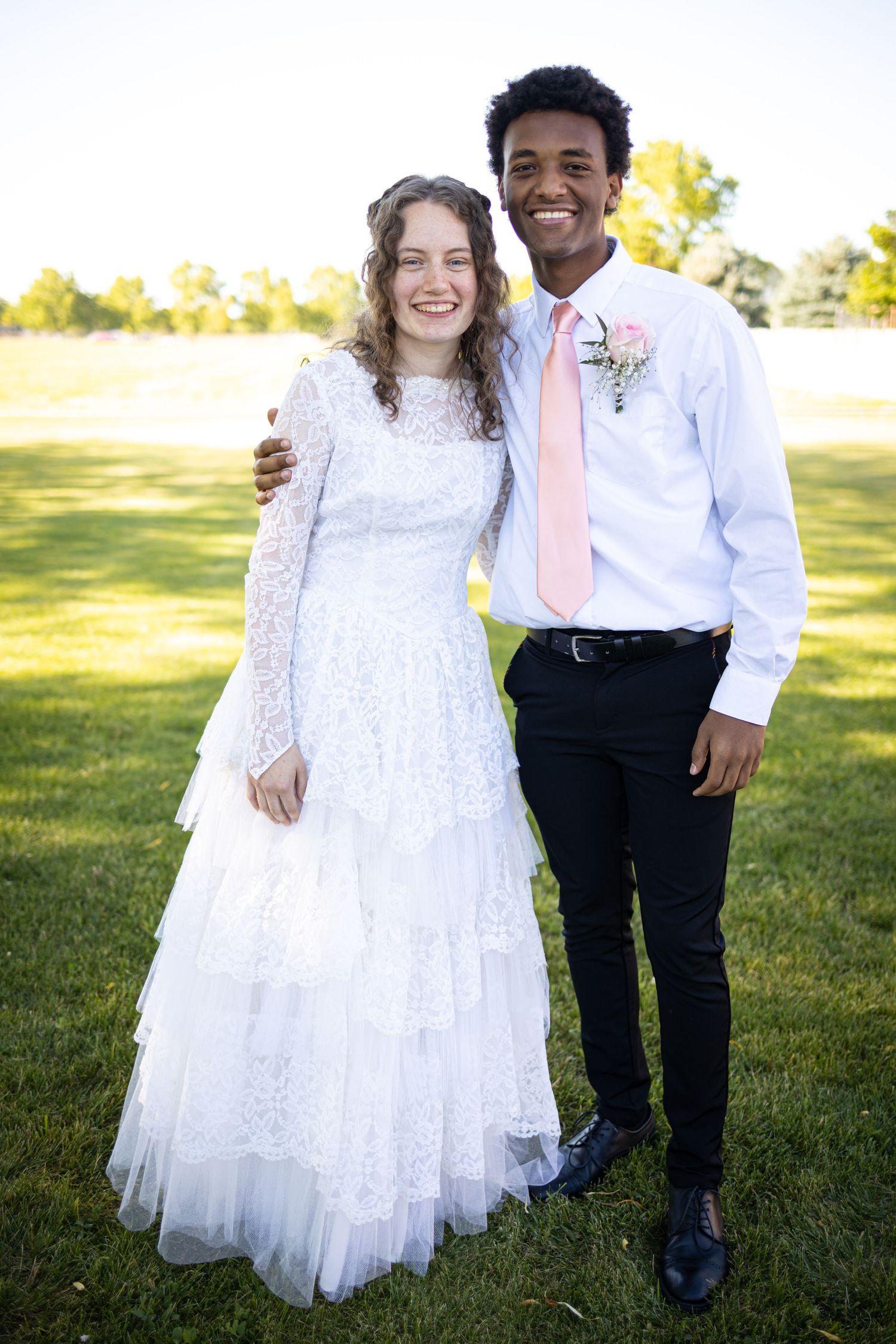 Happy couple stands together on sunny lawn in wedding attire.