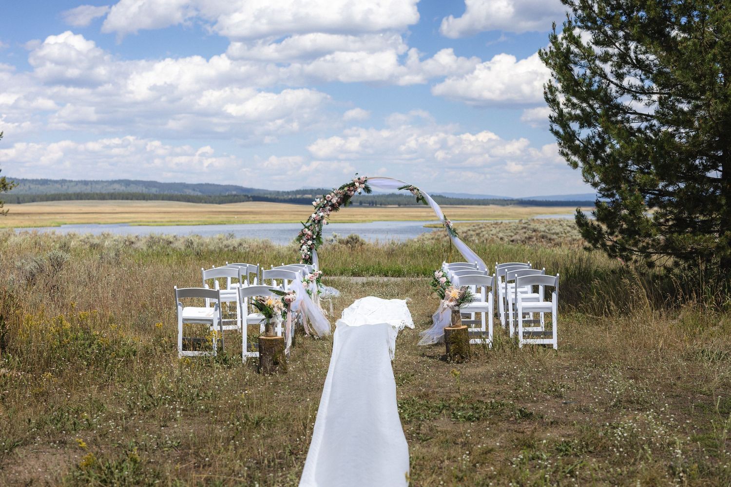 An outdoor wedding ceremony setup with a floral arch and white chairs against a scenic mountain backdrop.