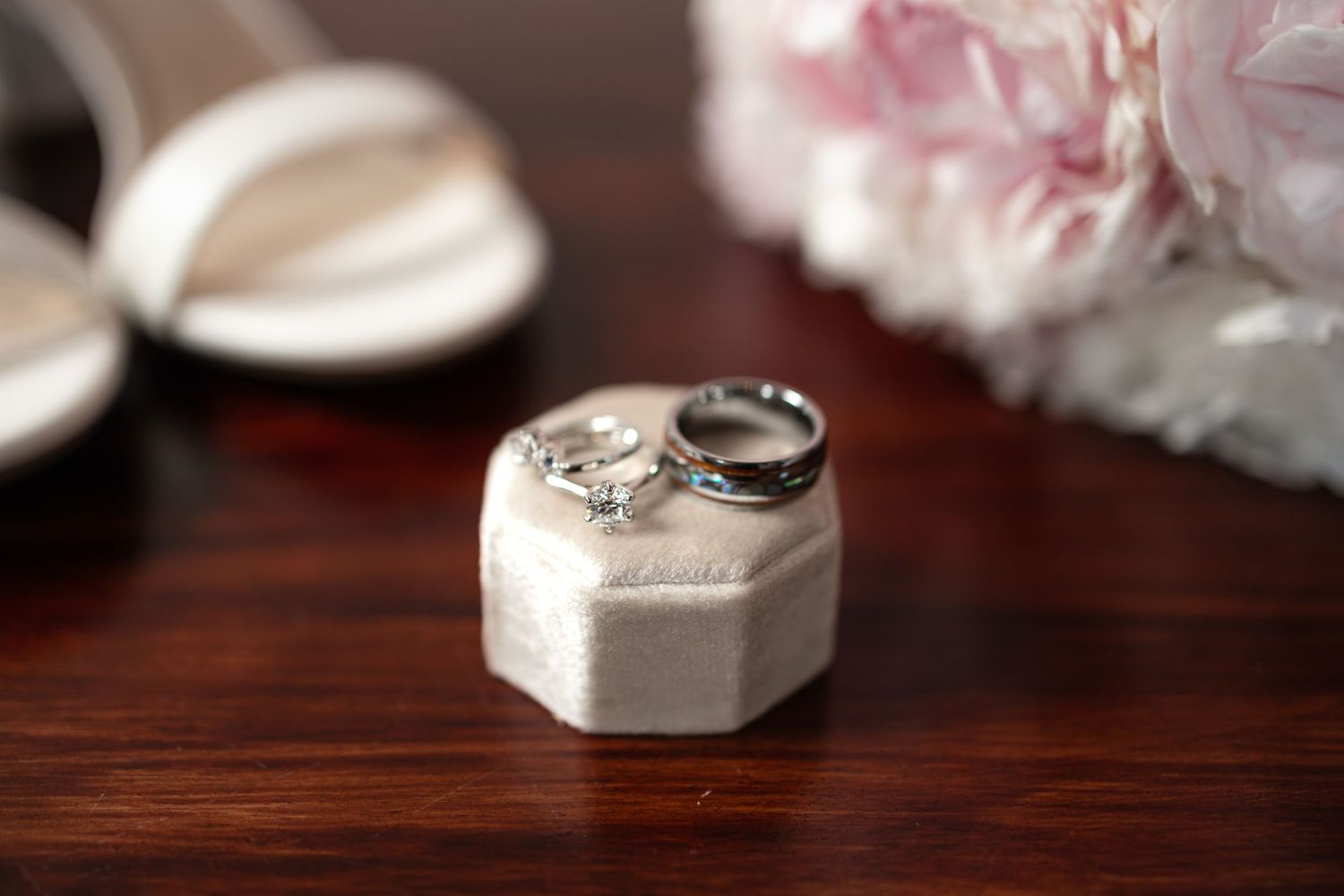 Diamond wedding rings in hexagonal box with soft focus floral background.