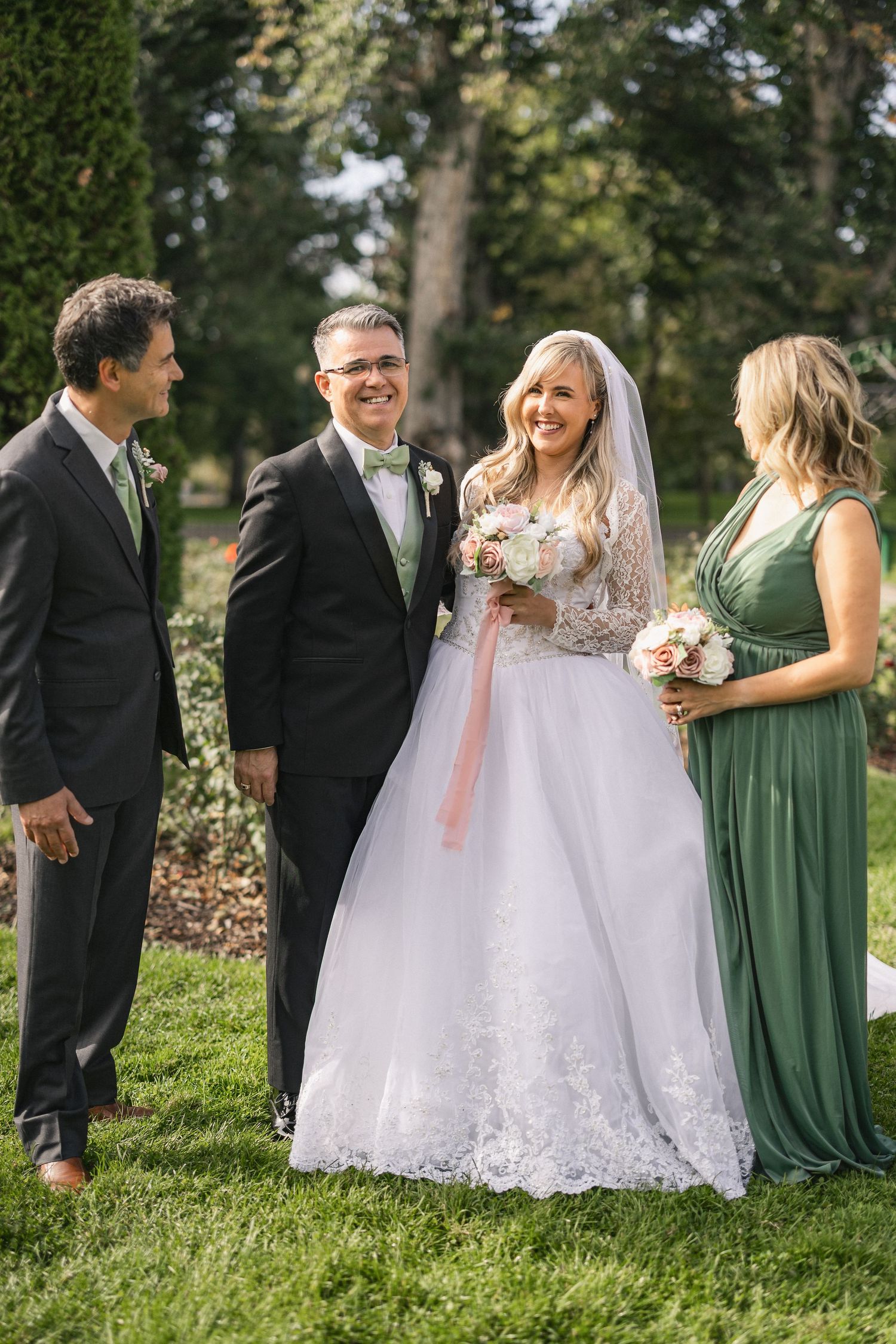 Wedding party members in formal attire gather for photos in a lush garden setting.
